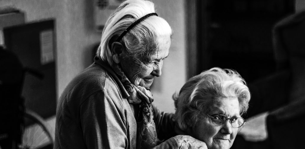 greyscale photo of woman standing behind woman sitting on chair